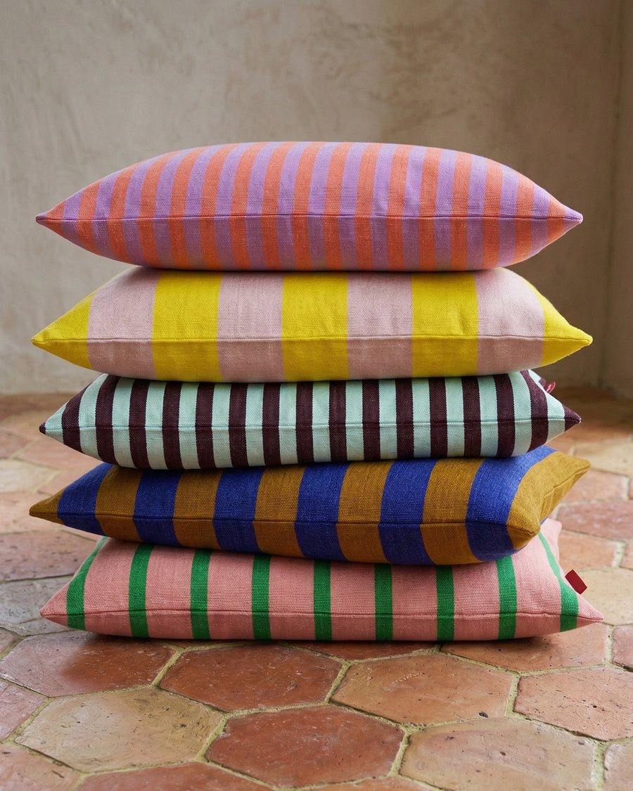 Stack of colorful striped pillows on a terracotta floor, available via Wildschut Antiques.