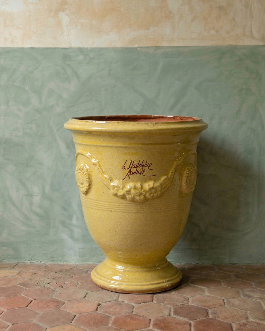 Yellow ceramic Anduze pot or jar with decorative elements against a textured wall, available via Wildschut Antiques.