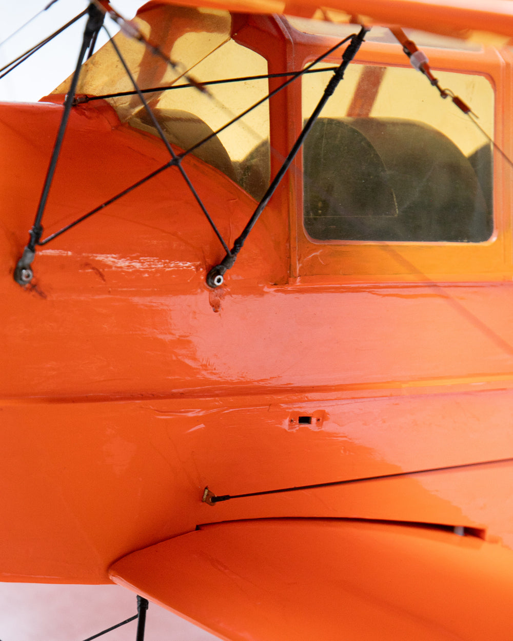 Close-up of an orange aircraft fuselage with a yellow-tinted canopy window and black struts.