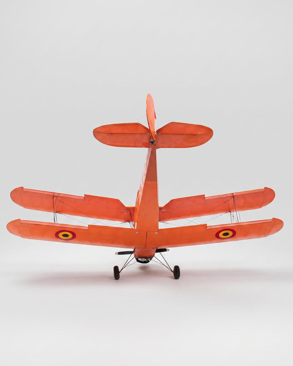 An orange model biplane aircraft photographed from the rear on a light gray studio background.