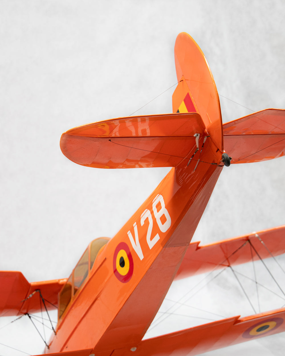 Close-up of an orange vintage biplane tail section with white V28 lettering markings against a light gray background.