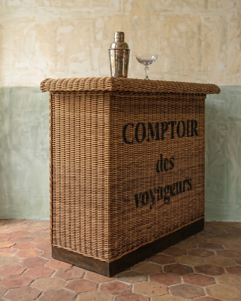 Wicker bar with 'Comptoir des Voyageurs' text against a textured wall.