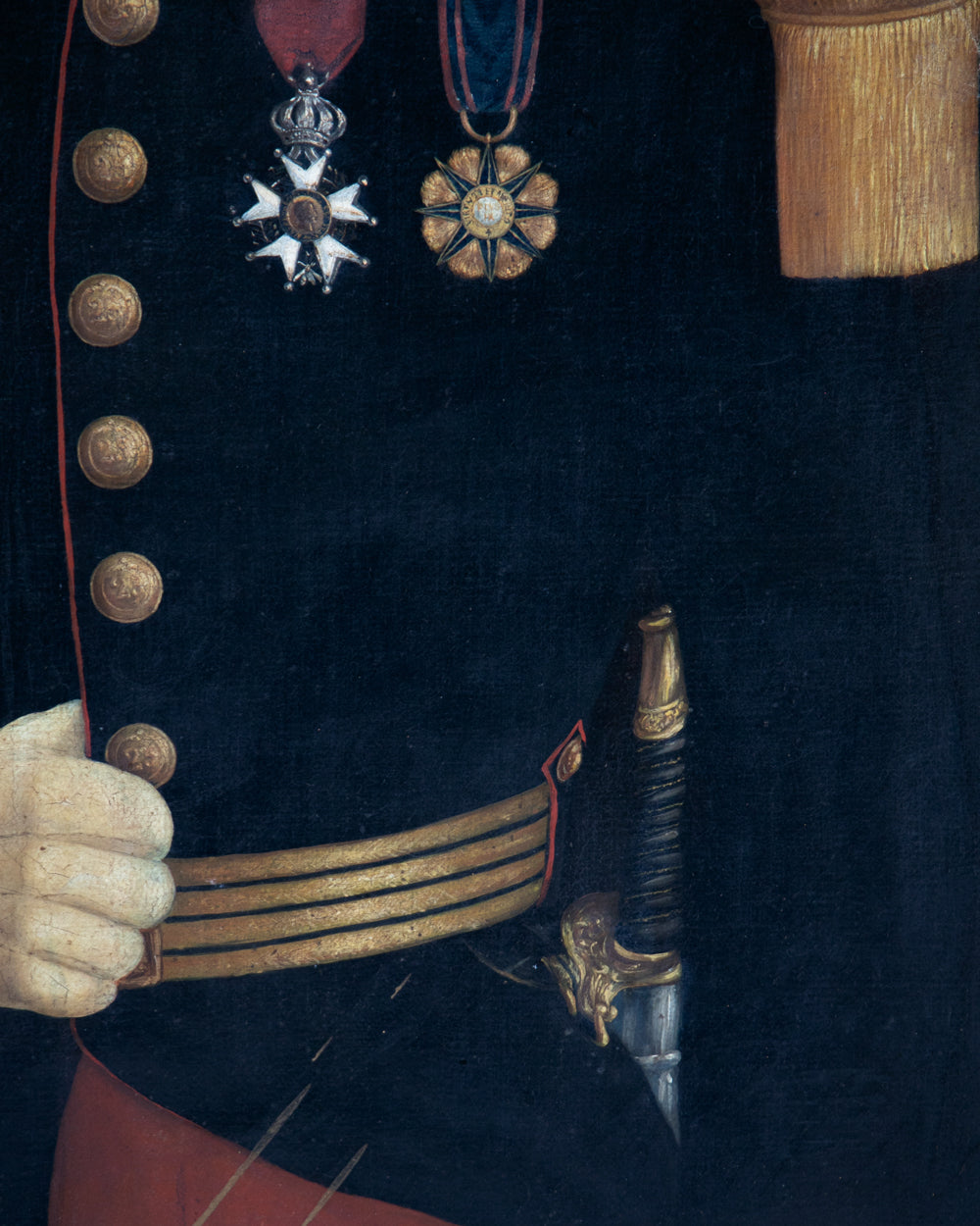 Close-up detail of a historical military uniform showing a dark navy jacket with gold buttons, medals, a gold belt, and a hand holding a sword hilt.