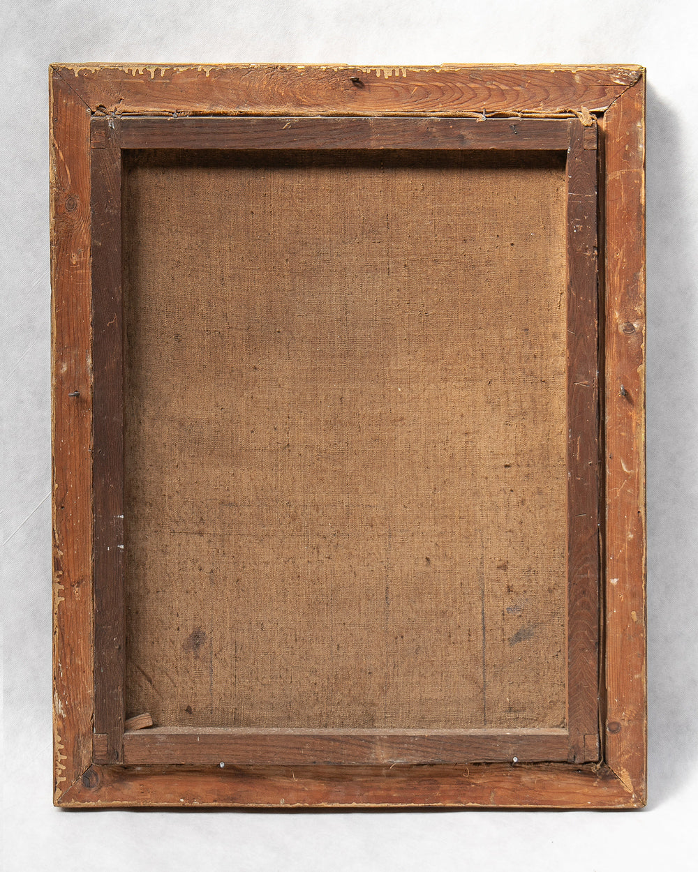 The back side of a rustic wooden picture frame, showing the canvas backing and corner pins, photographed against a light gray background.