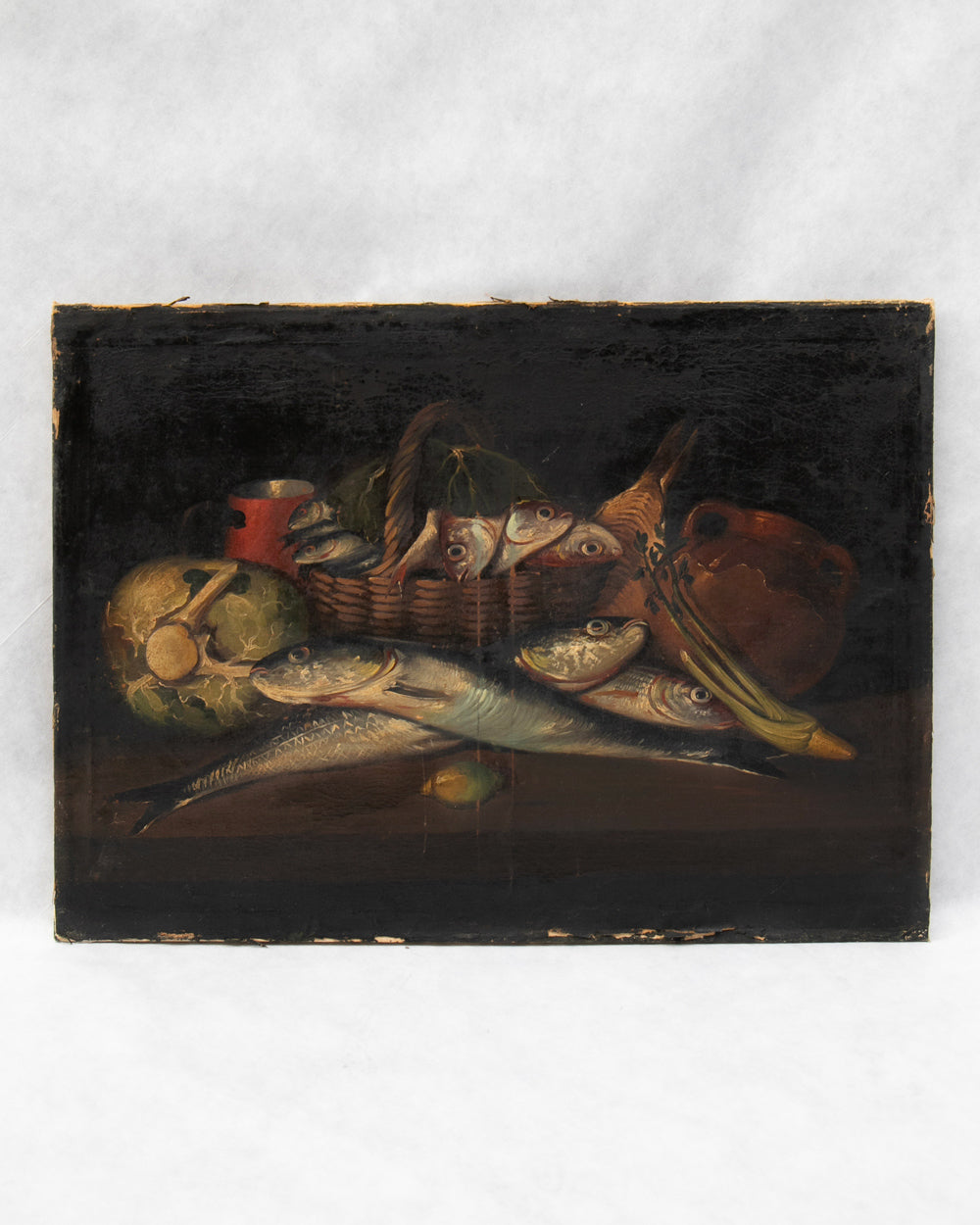 A rectangular oil painting depicting a still life of fish, a wicker basket, a red cup, and fruit on a dark background, shown against a light backdrop.