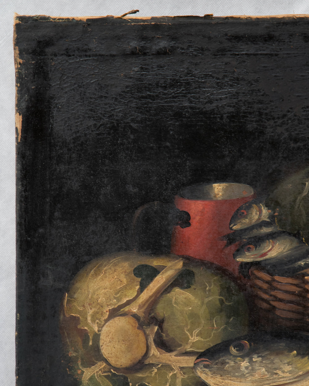 A close-up detail of a still life painting showing a red mug, fish, a round green object, and a basket against a dark background.
