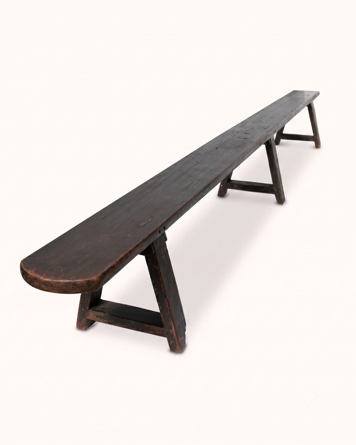 A long, dark brown wooden bench with a rounded front edge and A-frame legs, photographed on a plain off-white background.